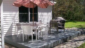 A covered patio with a table and chairs, a grill, and a large umbrella. - Suttons Bay-Pet Friendly-Walk to Brewery, beach, town, shops (Suttons Bay)