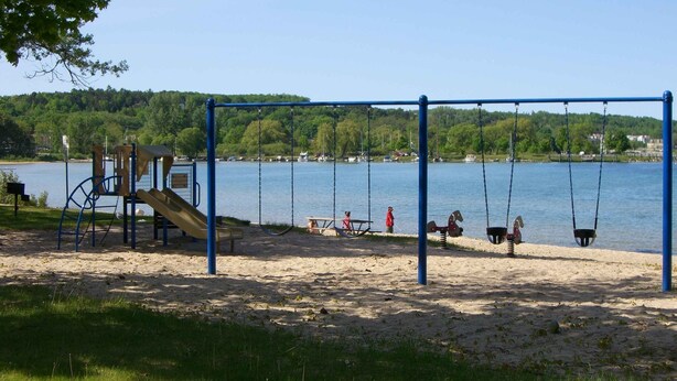 A playground with swings and a slide by a lake. - Suttons Bay-Pet Friendly-Walk to Brewery, beach, town, shops (Suttons Bay)