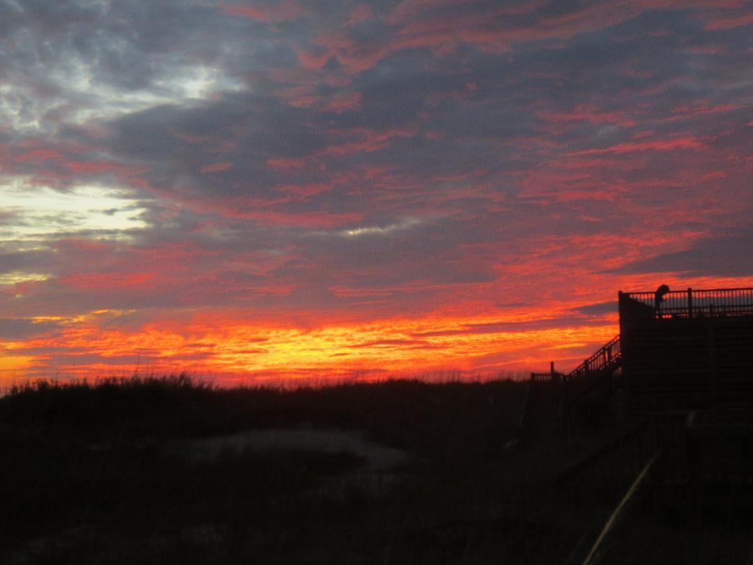 A sunset with a silhouette of a building and a fence.