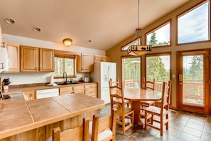 A spacious kitchen with wooden cabinets, a large island with seating, and a view through the glass doors. - Family Friendly Home w/ Game Room, Hot Tub, Telescope, Starlink Internet - Lunar View (Fairplay)