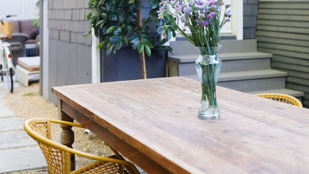 A wooden dining table with chairs, a vase with flowers, and a house in the background. - Central A/C, heat, Fireplace, Off-Street Parking, fenced yard (Santa Barbara)