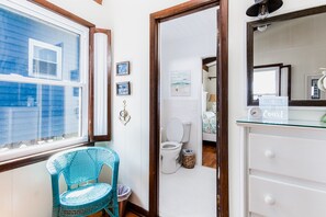 A bathroom with a white toilet, a wicker chair, a glass sink, and a "Take Time to Coast" sign.