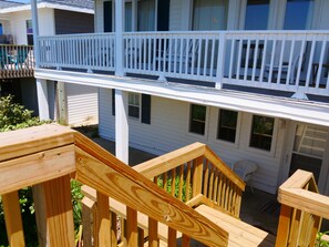 A wooden deck with a railing, a white balcony, and a window overlooking a garden.