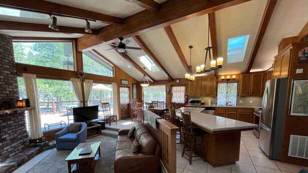 A spacious living area with a fireplace, a large sofa, a television, and a dining area with chairs and a table. - (48R) The Tree House II at The Redwoods In Yosemite (Yosemite National Park)
