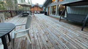 A wooden deck with outdoor furniture, a covered seating area, and a building with large windows in the background. - (48R) The Tree House II at The Redwoods In Yosemite (Yosemite National Park)