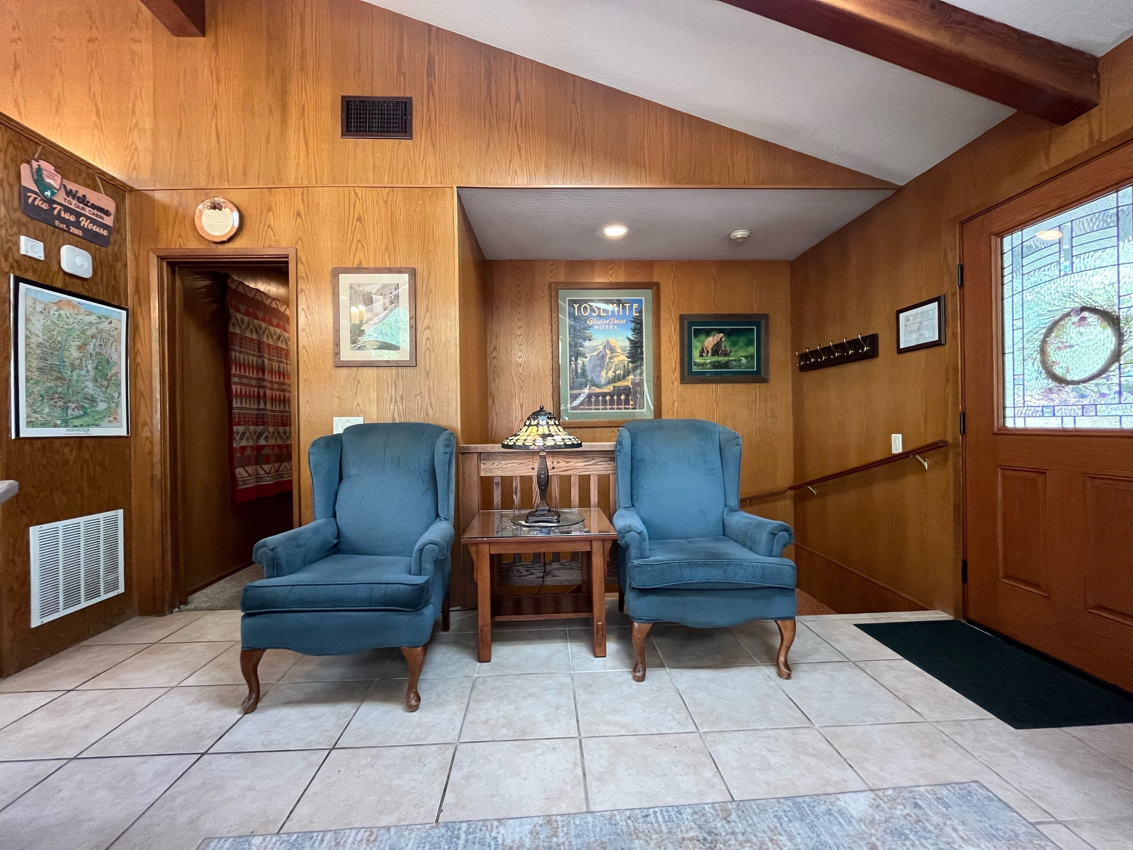 A wooden interior with two blue armchairs, a small table, and a poster on the wall.
