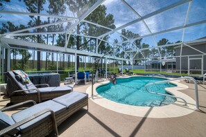 An outdoor pool area with lounge chairs and a hot tub under a covered structure.