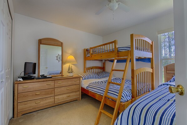 A bedroom with bunk beds, a dresser, a mirror, and a desk with a computer and lamp.