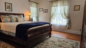 A bedroom with a wooden bed, floral curtains, and a nightstand with a lamp.