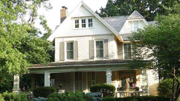 A two-story house with a stone facade, a front porch, and a chimney.