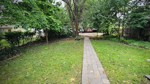 A paved pathway in a garden area with trees and grass.