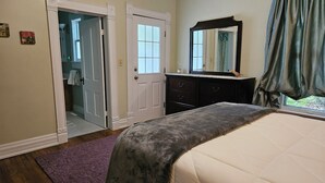 A bedroom with a bed, a dresser, a mirror, and a door leading to a bathroom.
