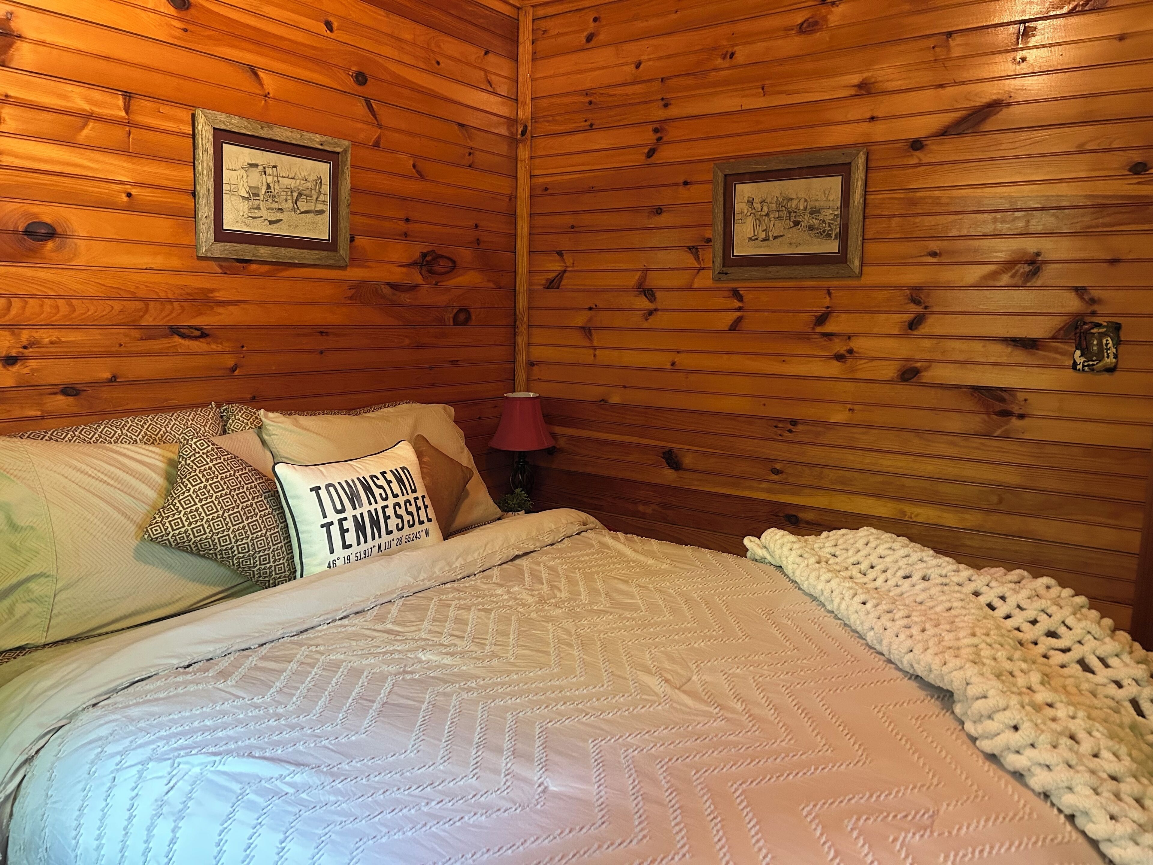 Ein Zimmer mit Holzwänden, einem Bett, Kissen und zwei gerahmten Bildern an der Wand.