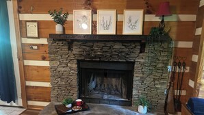 Una chimenea de piedra con una bandeja de galletas y una taza, fotografías enmarcadas en la parte superior y una pared de madera rústica.