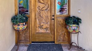 Une porte en bois ornée d’un bas-relief représentant un dauphin, flanquée de deux plantes en pot, qui donne sur un hall d’entrée carrelé.