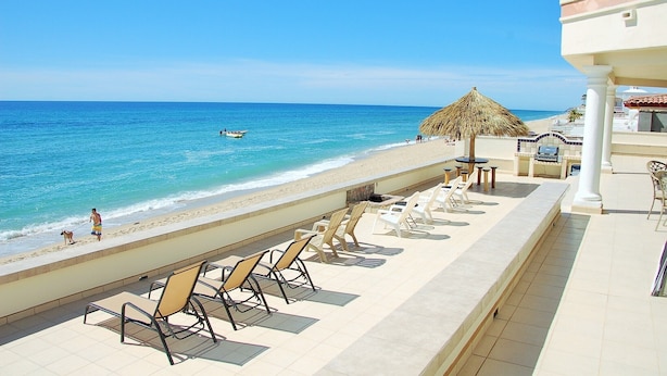 Une vue sur la plage, avec des chaises longues, un parasol en chaume et une vue sur l’océan.