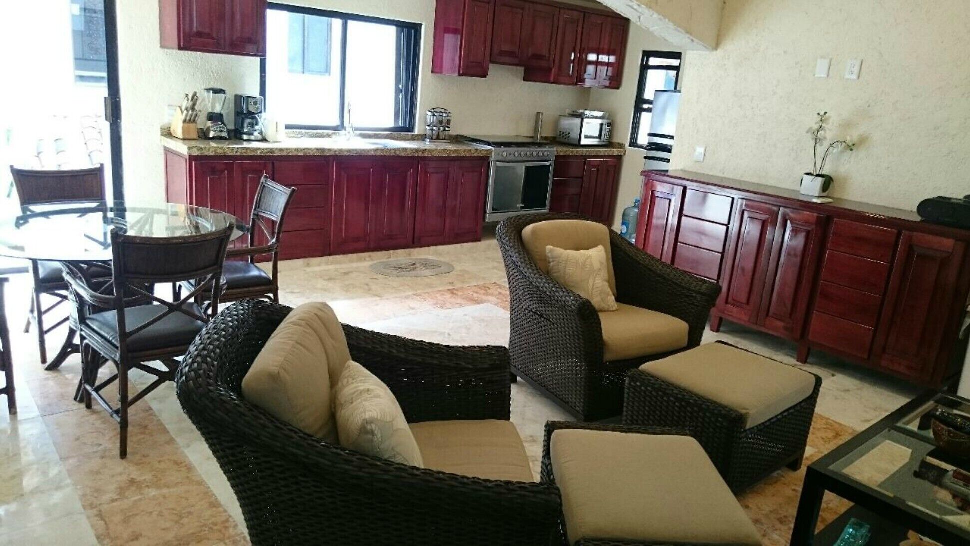A kitchen with red cabinets, a dining area with wicker furniture, and a large island with appliances.