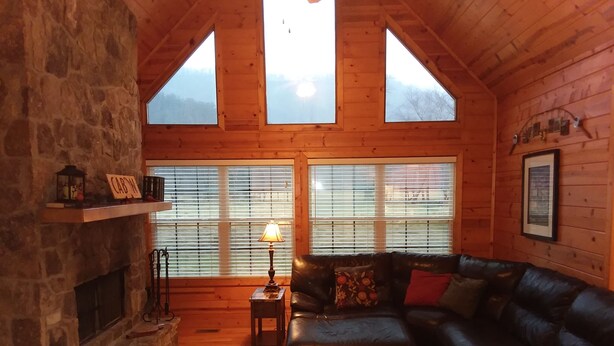 L’intérieur d’un chalet chaleureux, avec une cheminée en pierre, un canapé en cuir et une lampe.