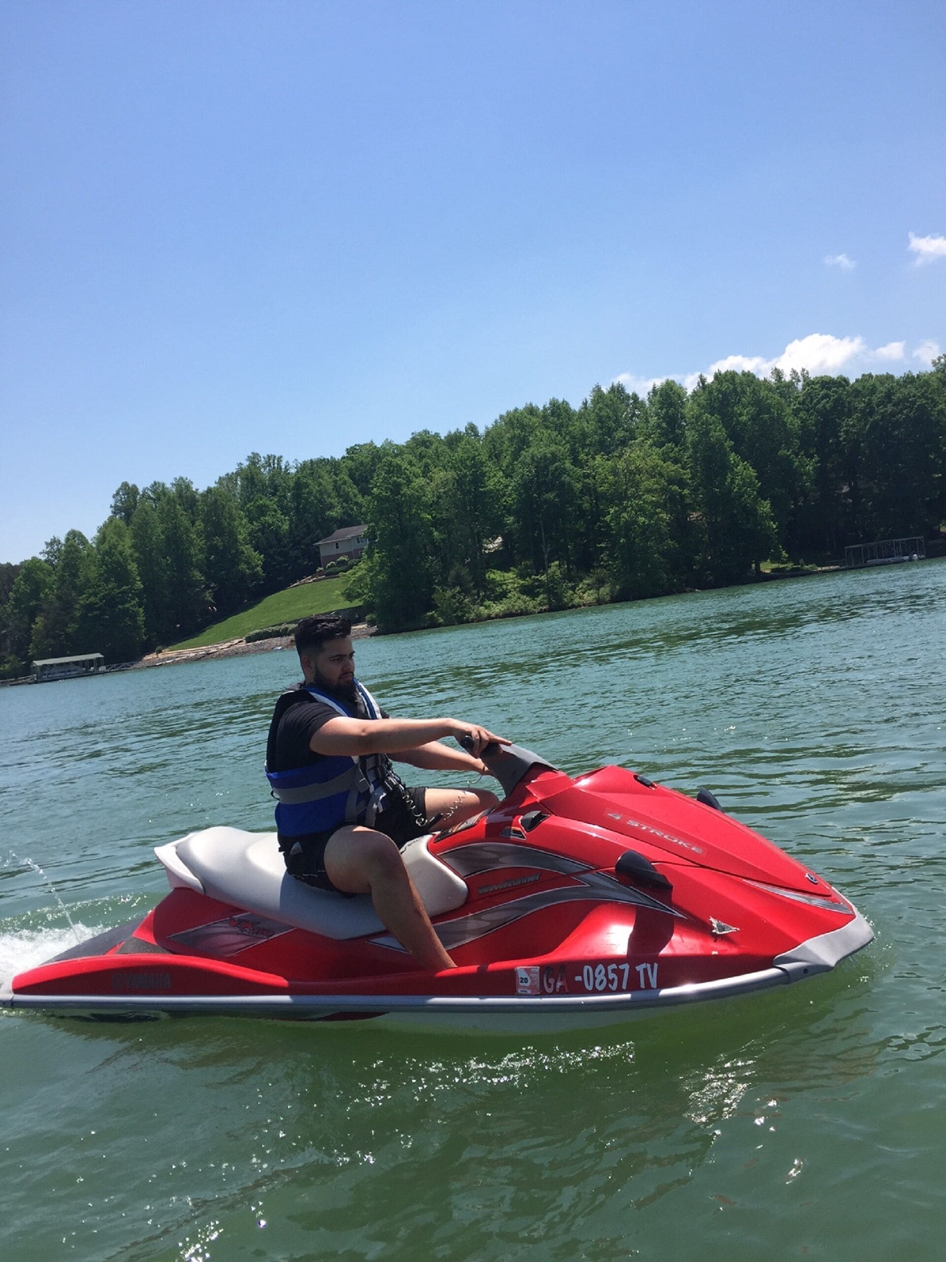 A person riding a red Yamaha jet ski on a lake with a forested shoreline in the background.