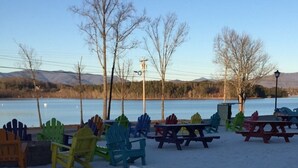 Une zone de plage avec des chaises Adirondack colorées et des tables de pique-nique, une plage de sable et un lac, avec des montagnes en arrière-plan.