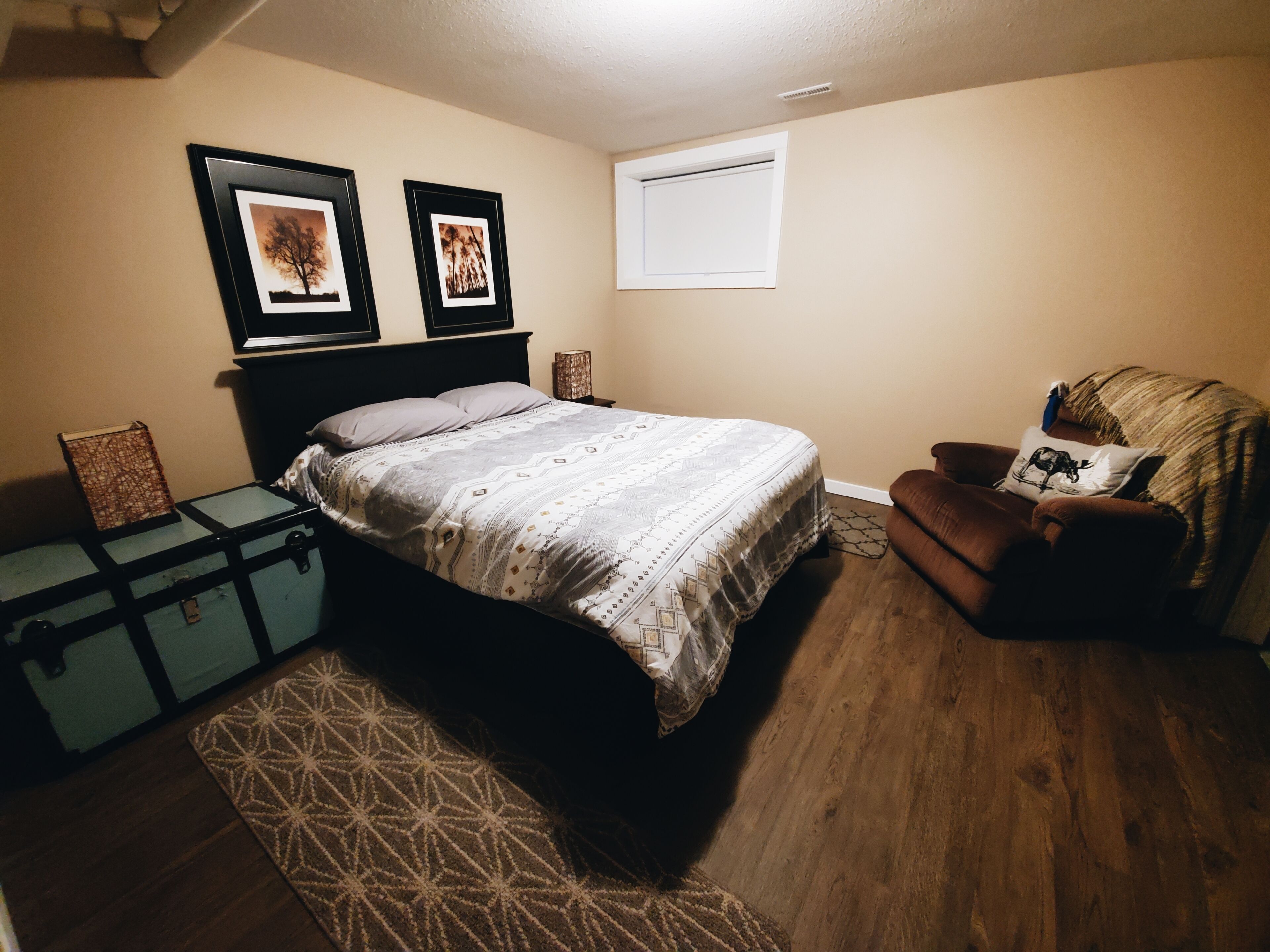 Une chambre à coucher avec un lit, une chaise, une valise et deux tableaux encadrés accrochés au mur.