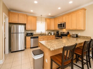 A modern kitchen with stainless steel appliances, wooden cabinets, granite countertops, and a central island with bar stools.