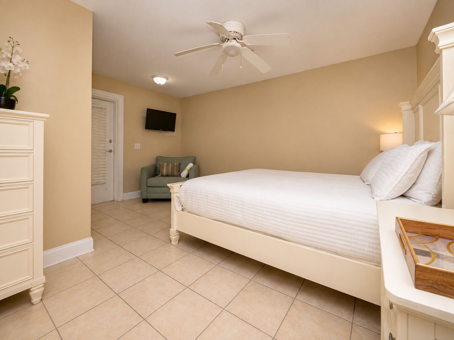 A bedroom with a bed, a dresser, a television, and a ceiling fan.
