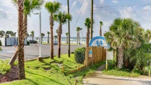 A beachside entrance with palm trees, a parking area, and a sign indicating a beach club. - Last Minute Rates, Beach Front Home, 3Beds, 3.5 Bath, Full Ocean View (Panama City Beach)