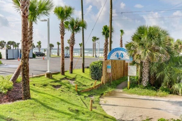 A beachside entrance with palm trees, a parking area, and a sign indicating a beach club. - Last Minute Rates, Beach Front Home, 3Beds, 3.5 Bath, Full Ocean View (Panama City Beach)