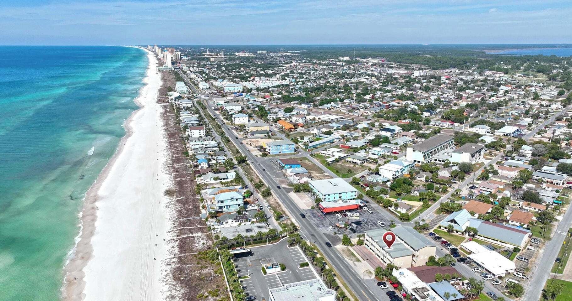 An aerial view of a coastal town with a beach, roads, and buildings.