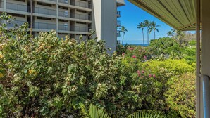 A hotel with a multi-story building, a covered outdoor area with greenery, and a view of the ocean. - Partial Ocean View, Pool, WiFi, Walk to Beach, ACs (Kihei)