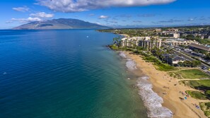 An aerial view of a coastal area with a beach, a mountain in the background, and a hotel complex with multiple buildings. - Partial Ocean View, Pool, WiFi, Walk to Beach, ACs (Kihei)