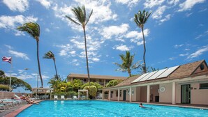 A swimming pool with lounge chairs, palm trees, and a building with a tiled roof. - Partial Ocean View, Pool, WiFi, Walk to Beach, ACs (Kihei)