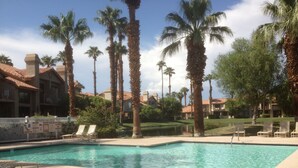 A swimming pool surrounded by palm trees and lounge chairs, with a building in the background. - 2BR PGA West Dog-Friendly Condo w/Stunning Lake and Mountain Views #248982 (La Quinta)