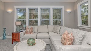 A living room with a sectional sofa, a round coffee table, and a side table with a lamp. - Charming cottage in Sabal Palm with screened in porch and outdoor shower (Bald Head Island)