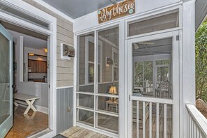 A covered porch with a sign reading "By the Sea." - Charming cottage in Sabal Palm with screened in porch and outdoor shower (Bald Head Island)