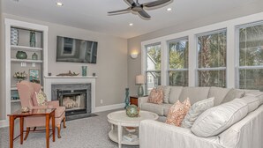 A living room with a fireplace, a sofa, a coffee table, and a TV mounted on the wall. - Charming cottage in Sabal Palm with screened in porch and outdoor shower (Bald Head Island)