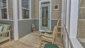 A covered porch with a wooden floor, a light blue door, and two rocking chairs. - Charming cottage in Sabal Palm with screened in porch and outdoor shower (Bald Head Island)