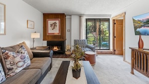 A living room with a fireplace, a sofa, a chair, a coffee table, and a television. - Best location in Breckenridge - Downtown - Ski In Ski Out - 1 Bedroom Condo (Breckenridge)