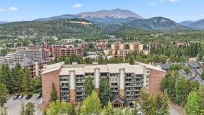 A multi-story hotel with a central courtyard, surrounded by dense forest and mountains in the background. - Best location in Breckenridge - Downtown - Ski In Ski Out - 1 Bedroom Condo (Breckenridge)