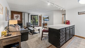 A modern kitchen with a large island, a dining area with a sofa and coffee table, and a living room with a fireplace. - Best location in Breckenridge - Downtown - Ski In Ski Out - 1 Bedroom Condo (Breckenridge)