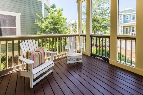 A wooden deck with two white Adirondack chairs, one with a striped cushion.