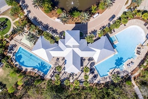 Ein Luftbild eines Resorts mit einem zentralen Gebäude, das ein sternförmiges Dach, zwei Swimmingpools und umliegende Palmen hat.