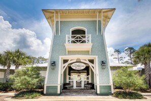A building with a green and white facade, a sign reading "The Gathering Place", and a gated entrance with benches outside.