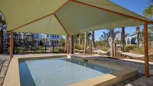 A swimming pool with a shaded area, surrounded by palm trees and houses.