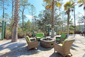 An outdoor patio area with wicker furniture, a stone fire pit, and a pergola structure.