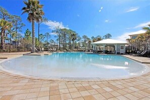 A swimming pool with lounge chairs and a gazebo, surrounded by palm trees and a clear sky.