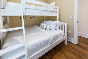 Una cama litera con ropa de cama y almohadas blancas, un adorno de pez en la pared y suelo de madera.