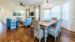A dining area with a wooden table and wicker chairs, a ceiling fan, and a chandelier.