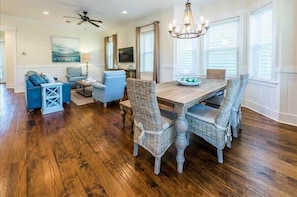 A dining area with a wooden table and wicker chairs, a ceiling fan, and a chandelier.